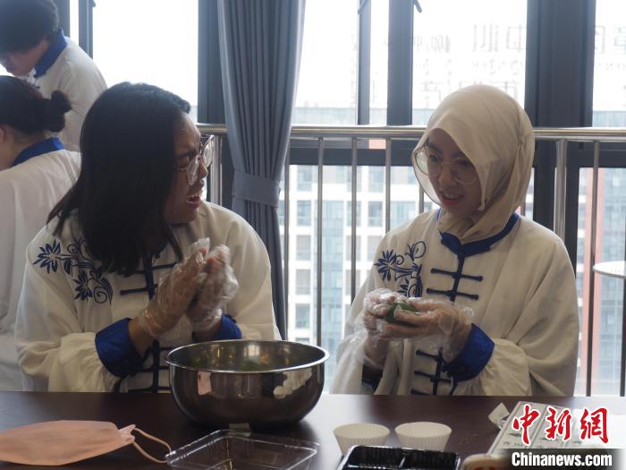 图为两名留学生一边制作青团一边交谈。　李娇阳摄